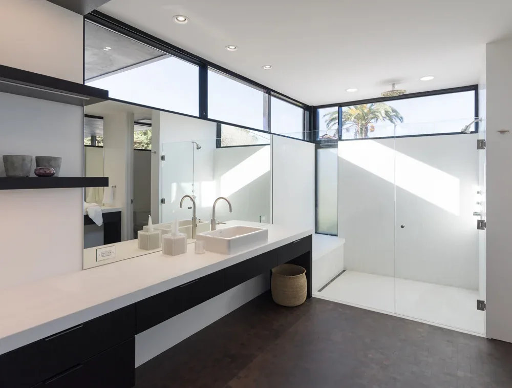 Modern bathroom features a double vanity with under-mounted sinks and a spacious walk-in shower with glass walls under clerestory windows.