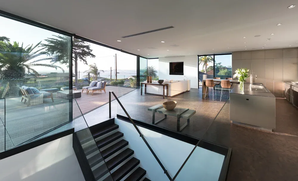 Neptune House features an open living space with floor-to-ceiling glass windows framing ocean views and seamless access to outdoor lounging areas.