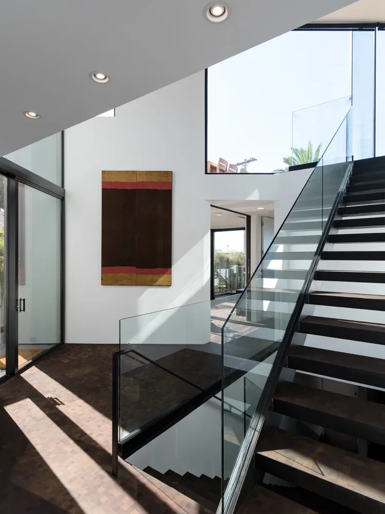 Modern stairwell in Neptune House featuring glass balcony railing and natural light from large windows.