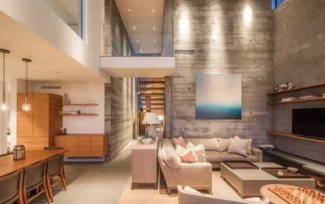 Living room of the Levine House features a double-height raw concrete wall with integrated shelving and adjacent dining area with wood paneling.