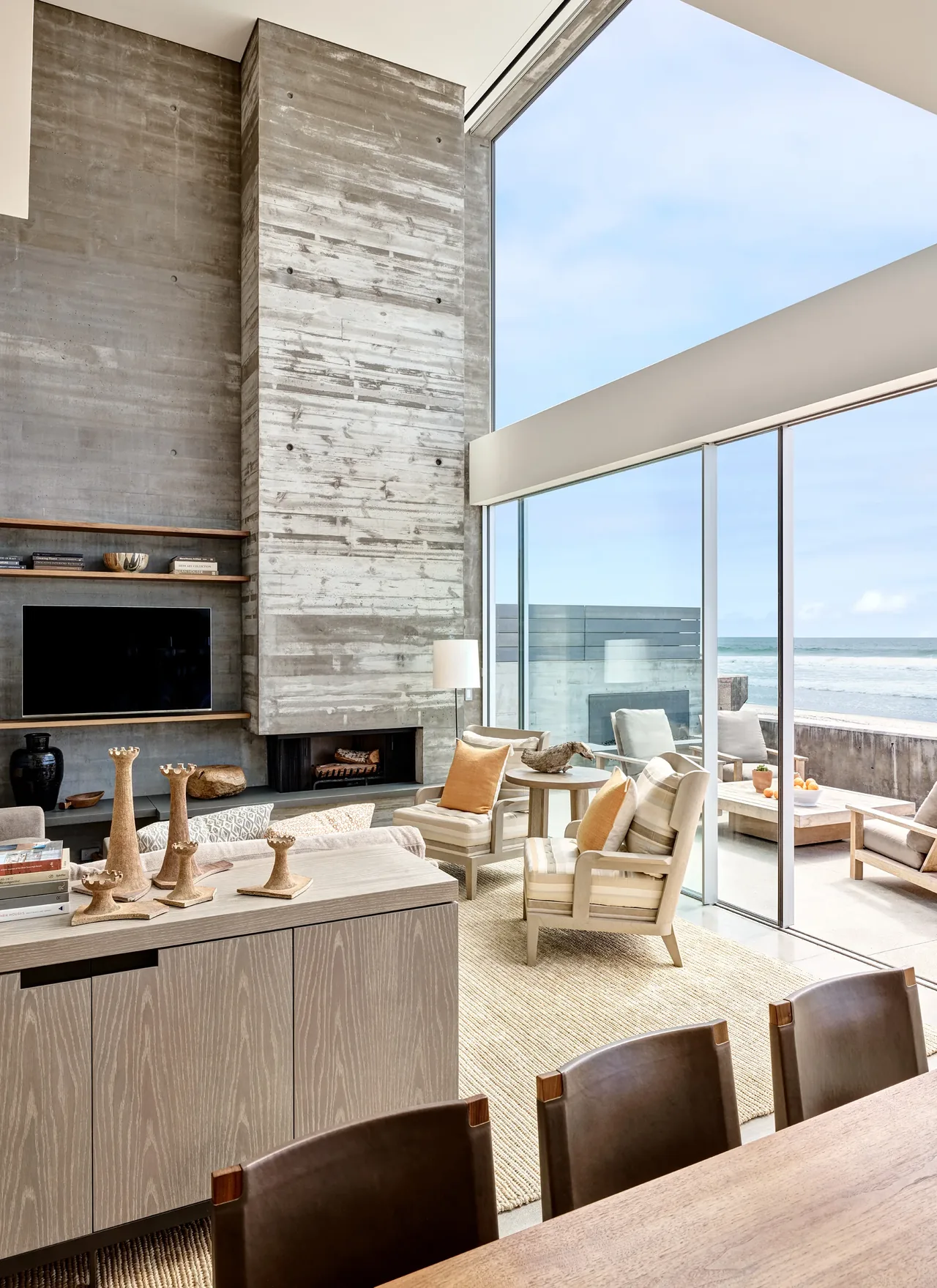Levine House living room features a tall raw concrete fireplace and expansive sliding glass doors opening to the ocean.