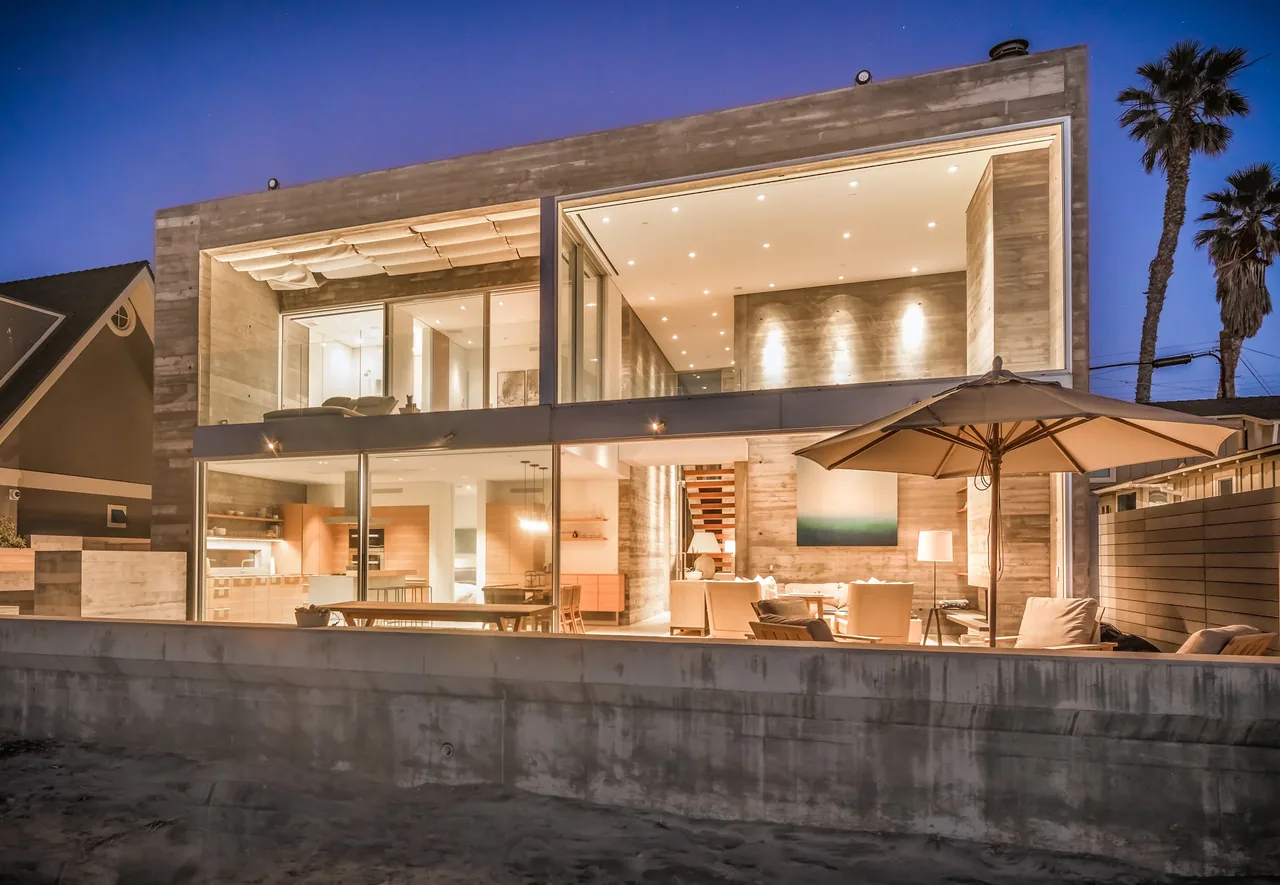 The Levine House features floor-to-ceiling glass walls and concrete exterior with an open patio space under soft evening lighting.