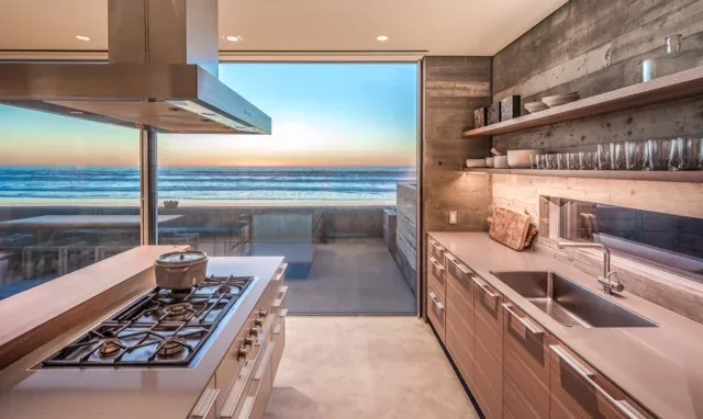 Kitchen in the Levine House by Batter Kay Associates features a concrete backsplash, wood cabinetry, and an expansive ocean view.