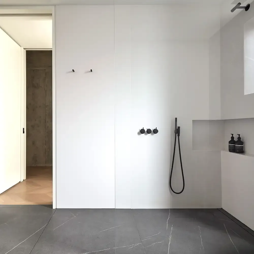 Bathroom features a minimalist design with black wall-mounted shower controls and a handheld shower head.