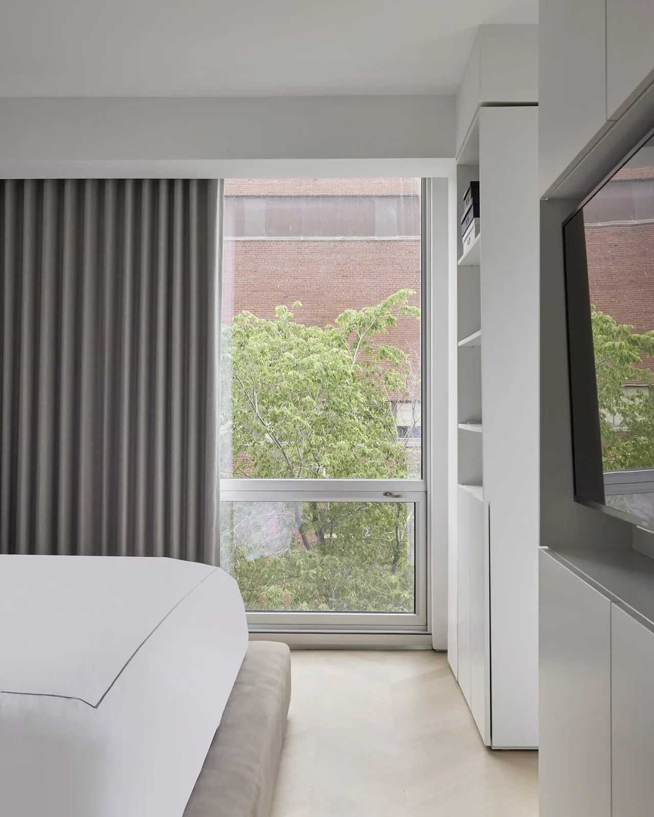 Modern bedroom corner with floor-to-ceiling window and built-in storage cabinetry.