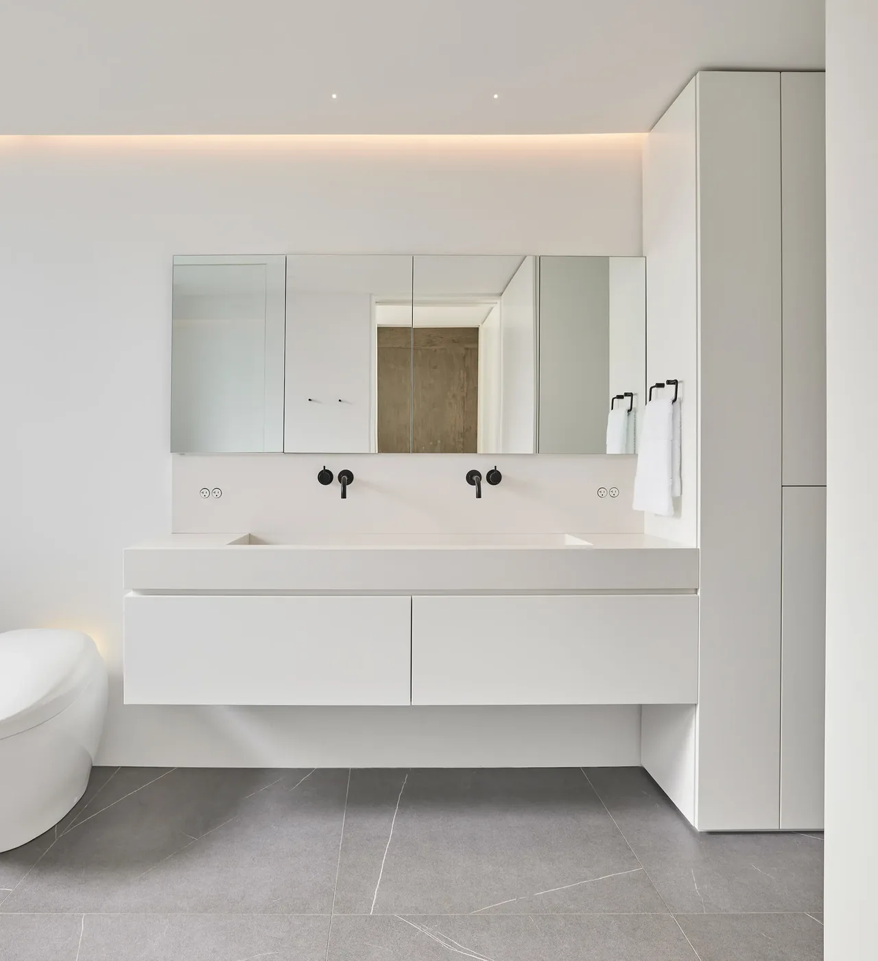 Minimalist bathroom featuring a floating vanity with dual black wall-mounted faucets and mirror cabinets.