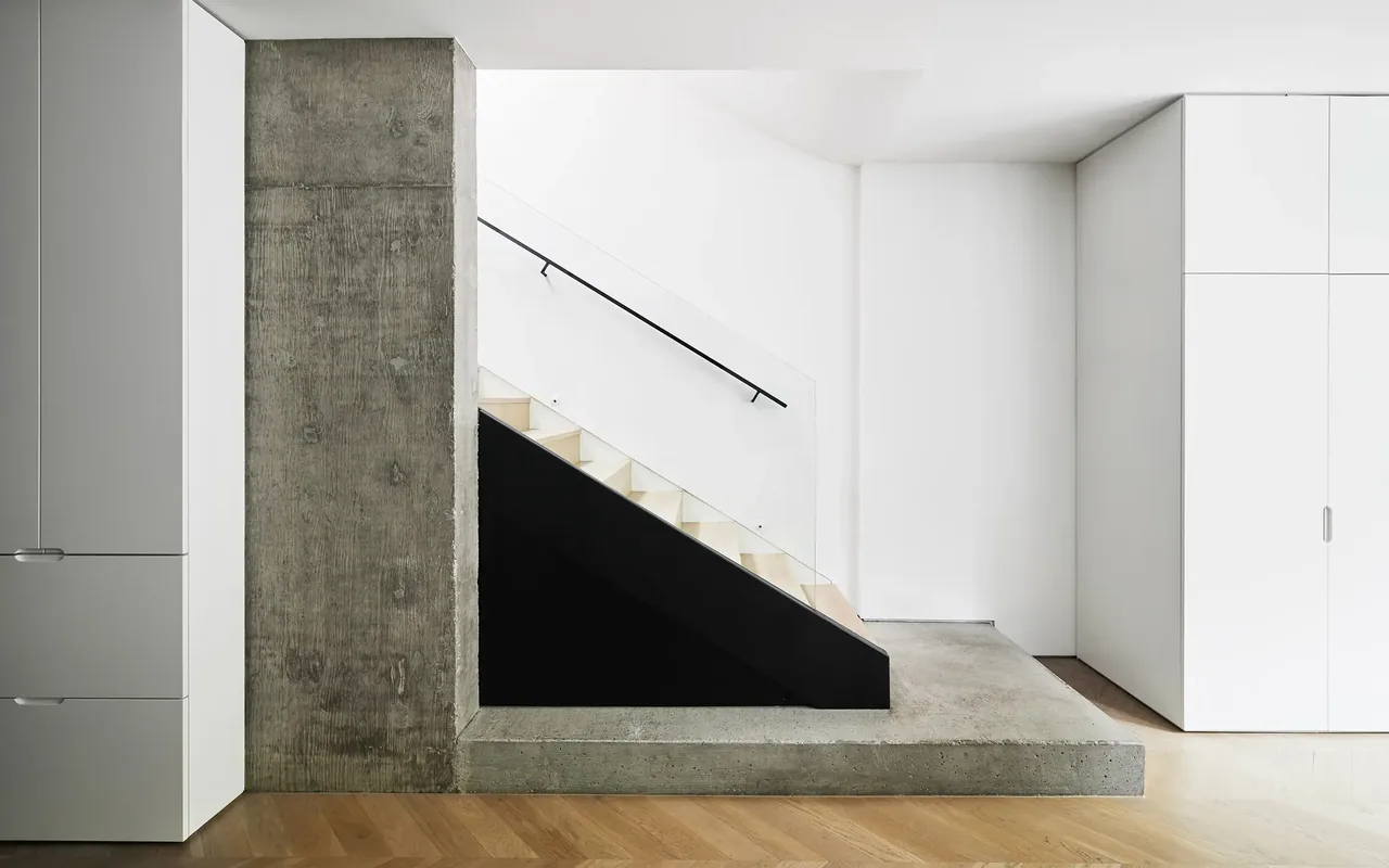 Modern interior view of a staircase framed by a concrete wall and platform with white cabinetry on each side.