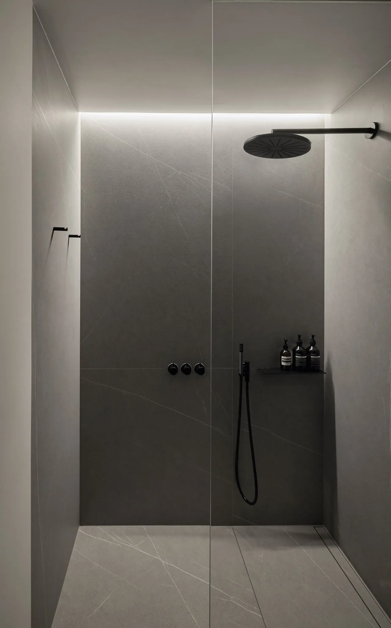 A minimalist shower features dark gray stone tiles with a black rain showerhead and recessed lighting.