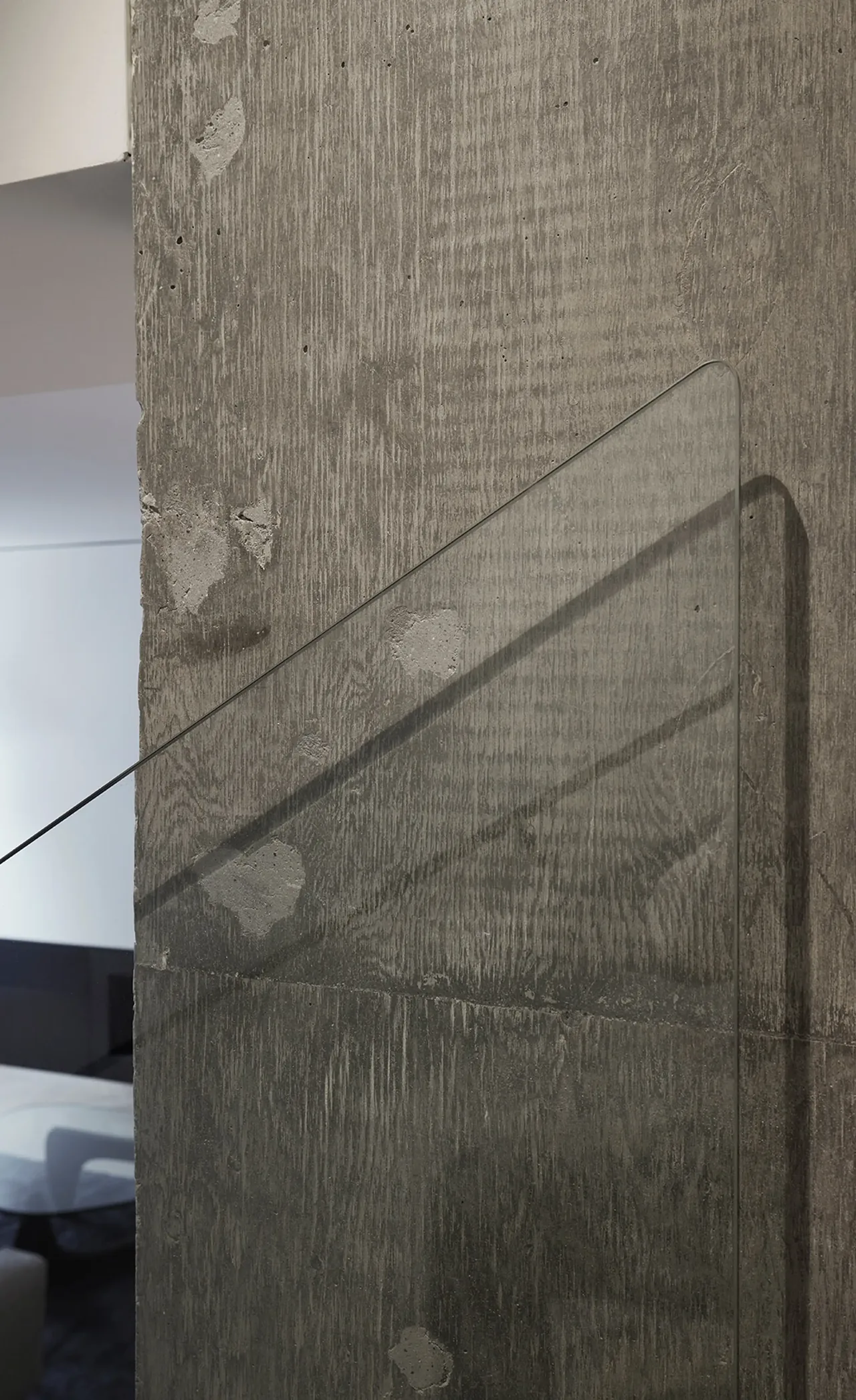 Concrete feature wall with wood grain texture and a transparent glass panel casting diagonal shadows.