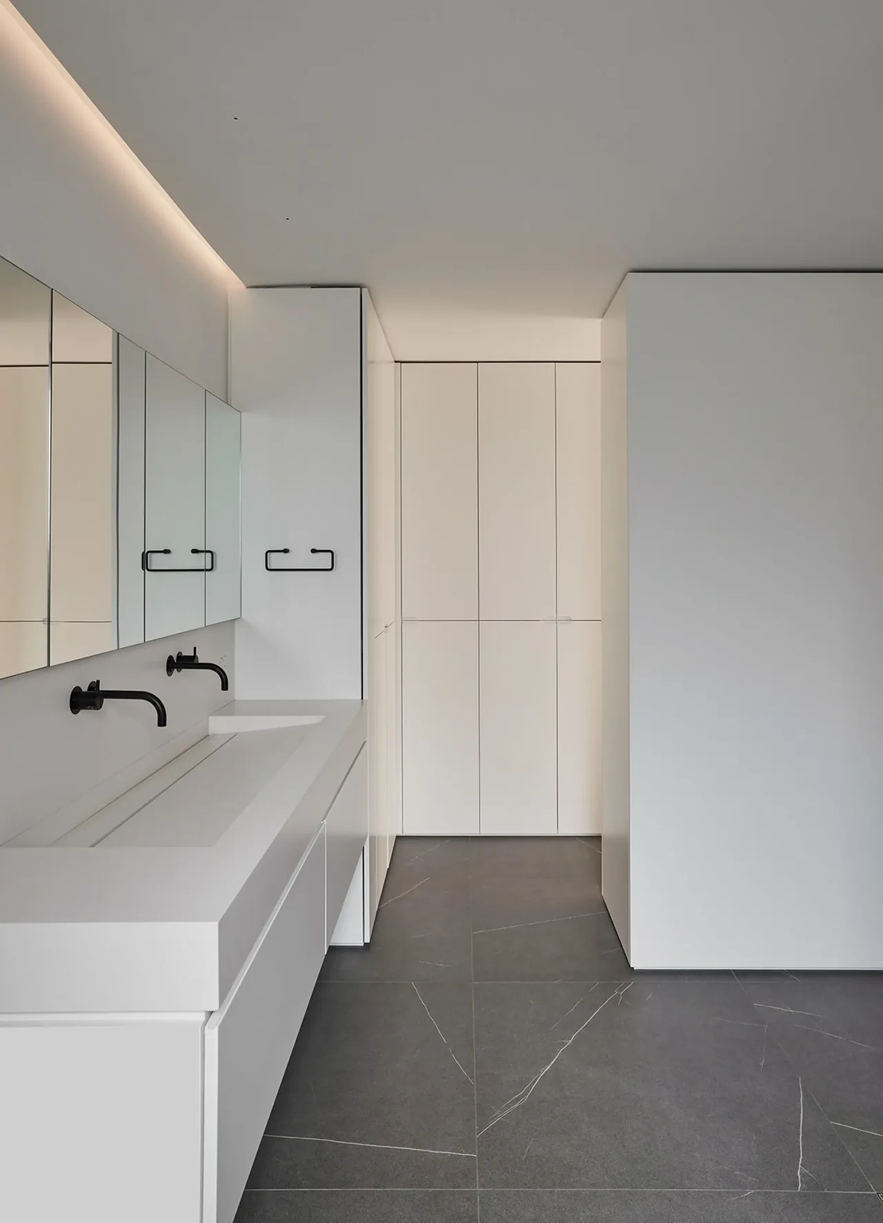 White minimalist bathroom featuring black wall-mounted faucets and integrated double sink on white cabinetry.