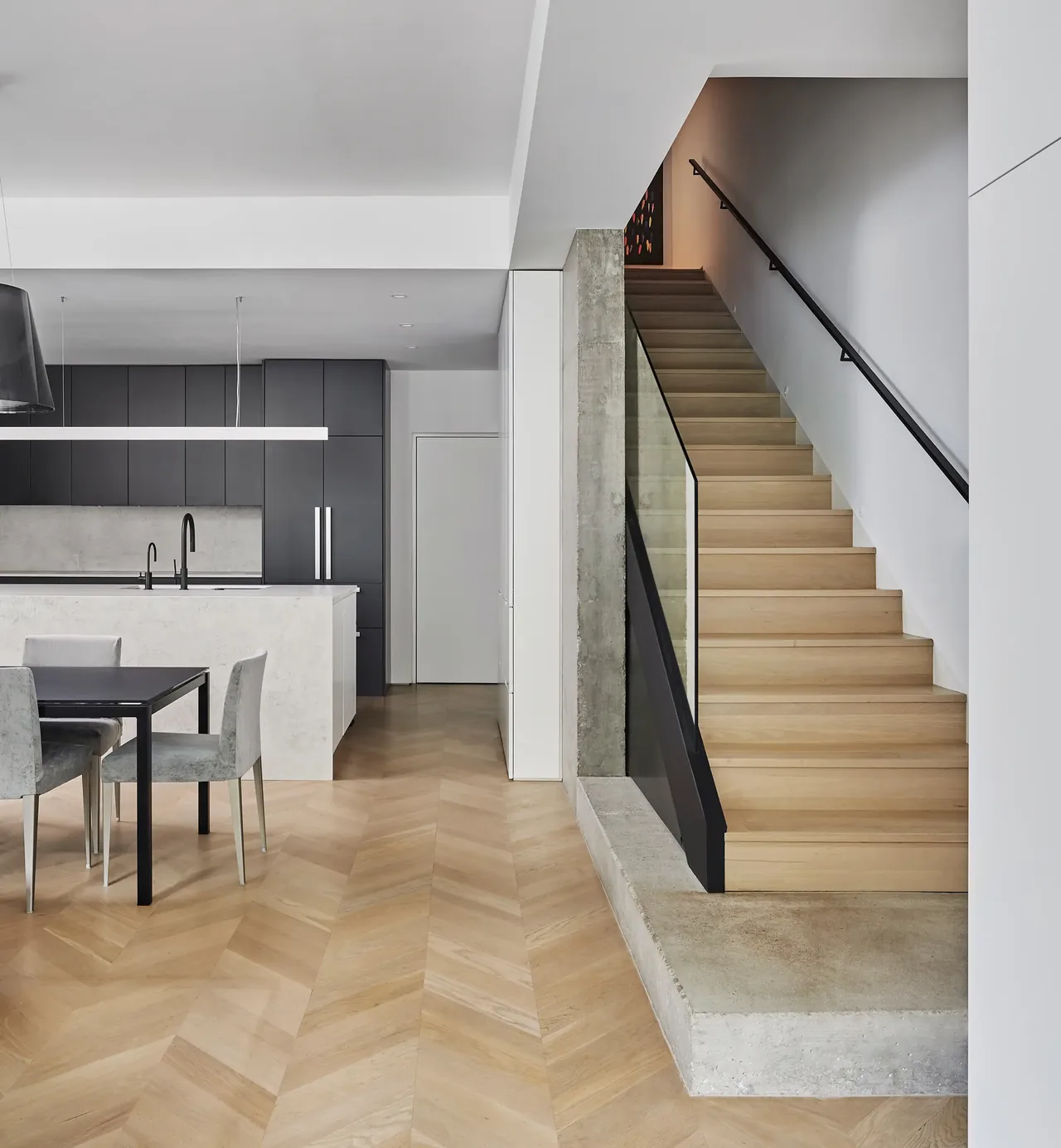 Kitchen and stair area with herringbone wood flooring, concrete platform, and black fixtures in a minimalist style.