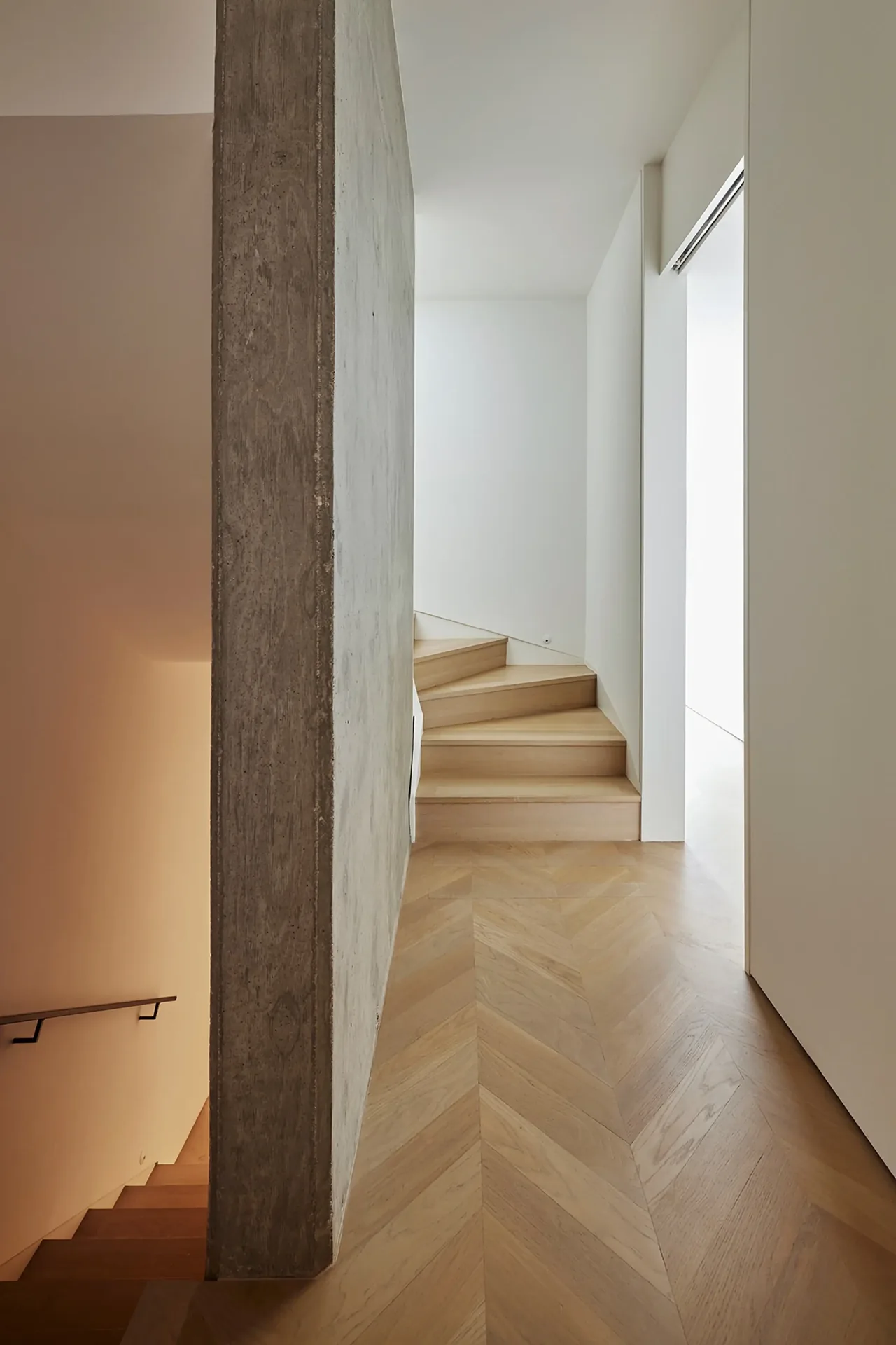 Hallway with herringbone oak floor, exposed concrete wall, and wooden stairs in Soldier Field House.