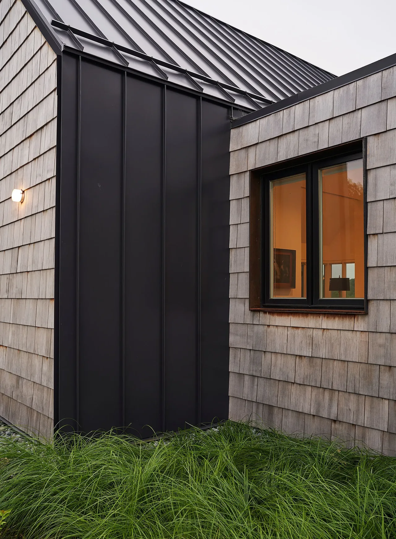 Exterior detail showing the combination of beige shingle siding and black vertical metal panels with rectangular windows at Lake Geneva House.