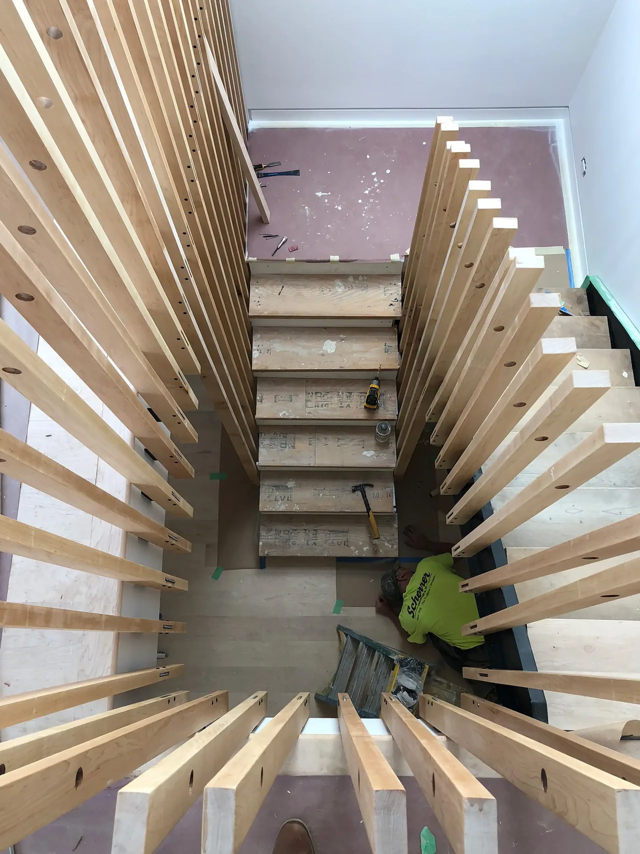 A stairway in mid-construction with exposed vertical wooden slats on both sides and unfinished steps.