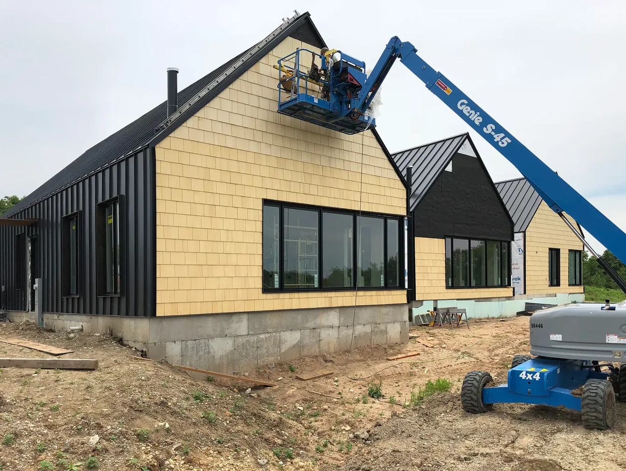 Lake Geneva House in construction showing beige shingle and black metal siding with tall rectangular windows and black window frames.
