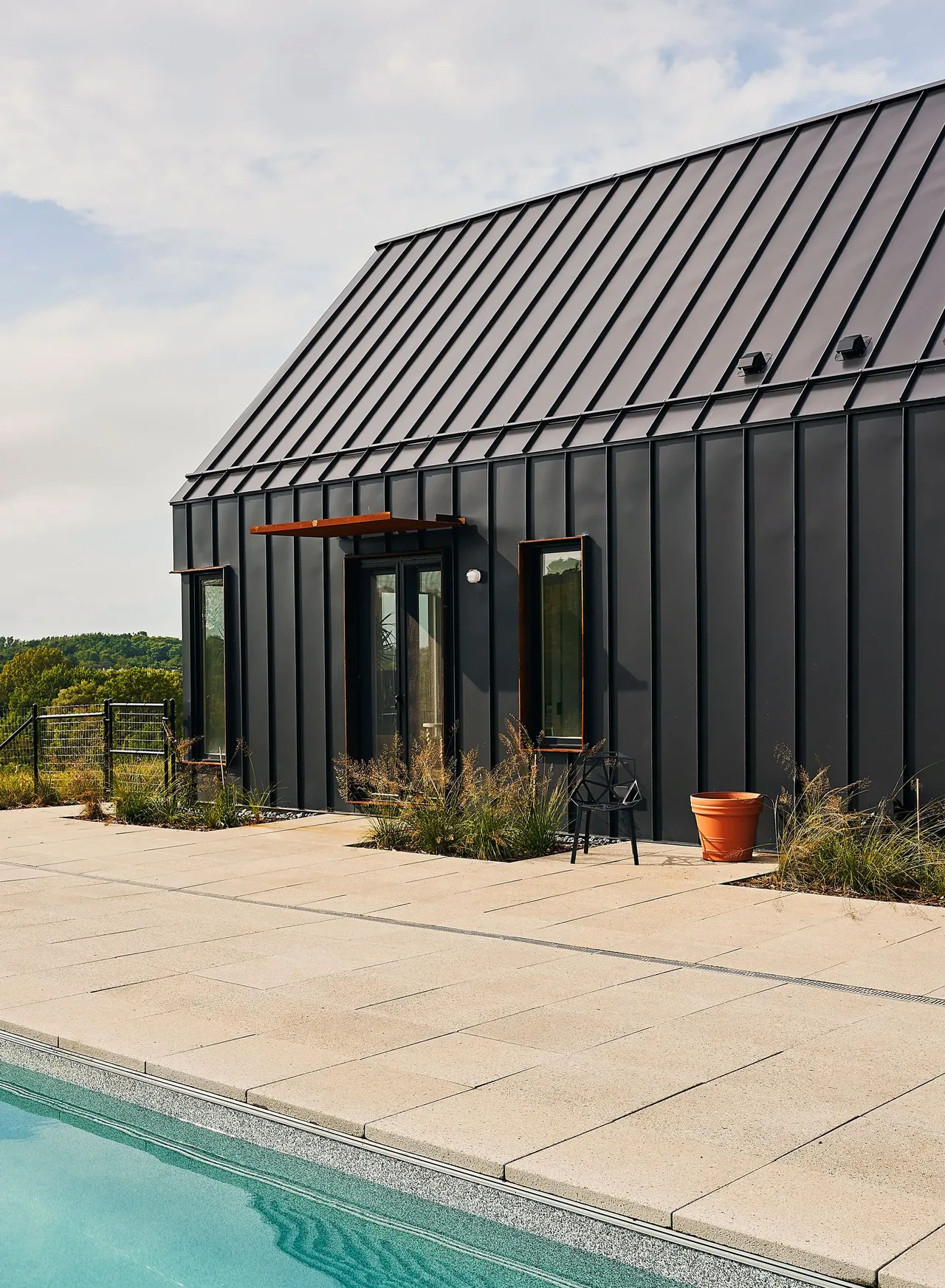 Exterior view of a modern build with black vertical metal siding and a poolside patio.