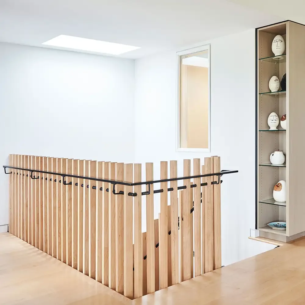 Upper hallway features vertical wooden slats for the staircase railing with a black metal handrail and a skylight above.