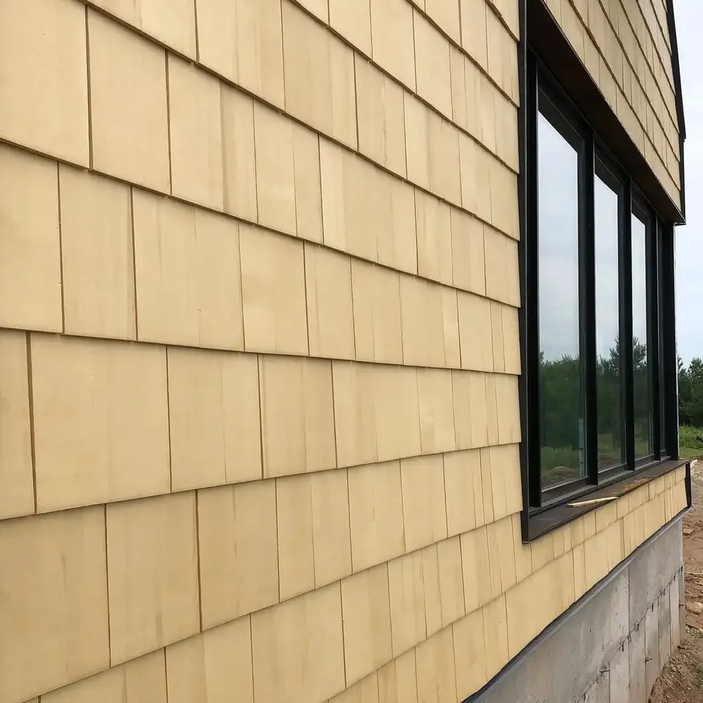 The exterior wall of the Lake Geneva House features beige wooden shingles with black window frames.