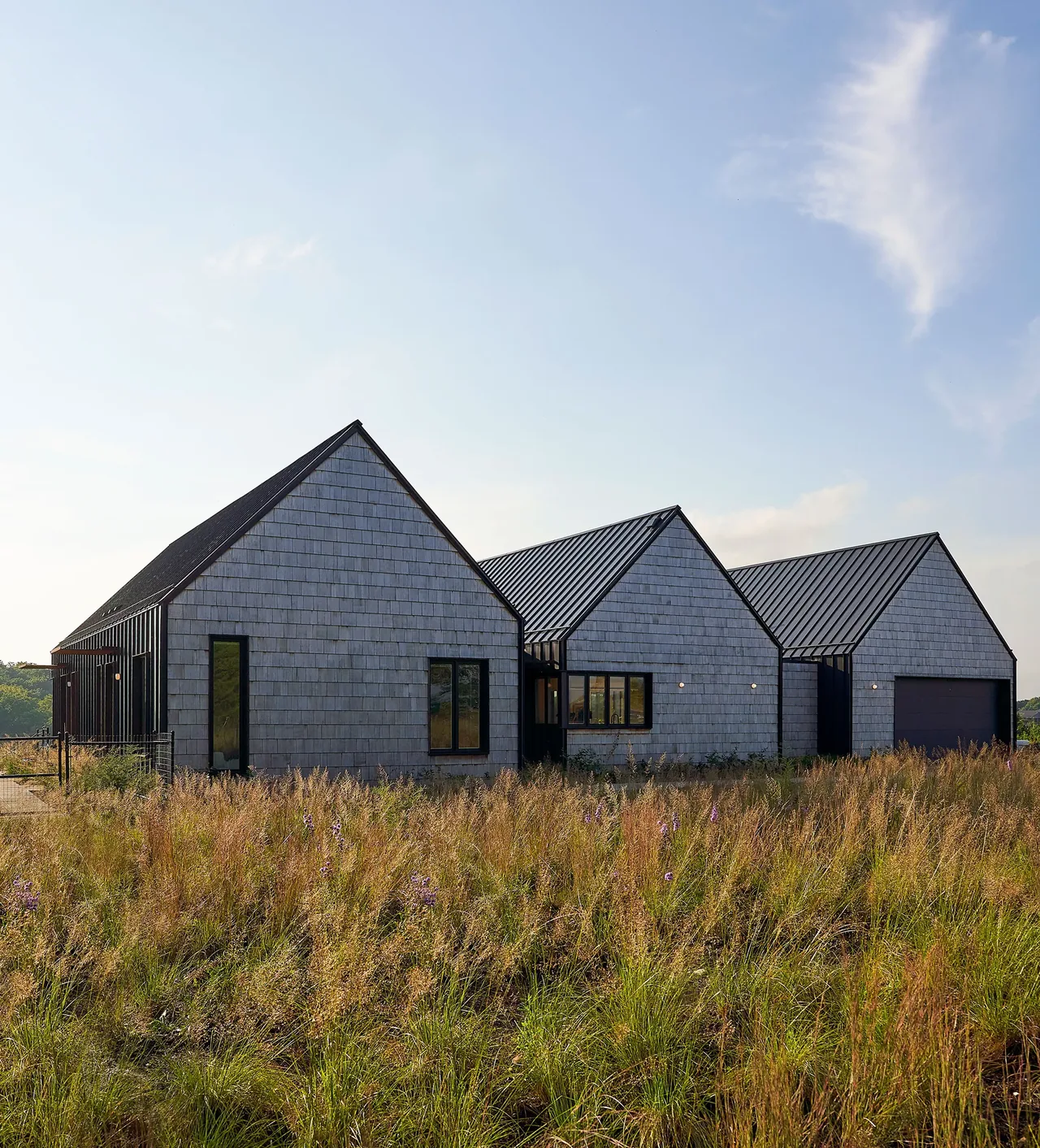 Lake Geneva House features connected pavilions with beige shingle siding and black metal pitched roofs.