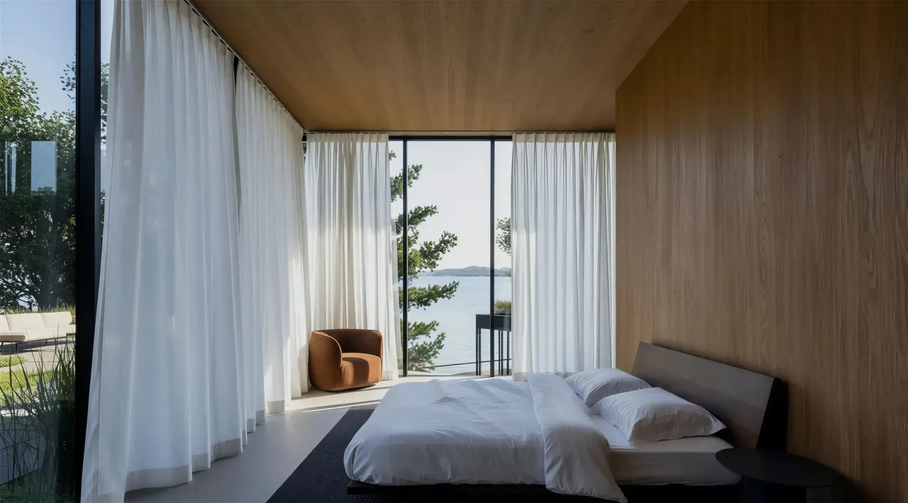 The Lakeside House bedroom features floor-to-ceiling glazing with views of the lake, wood-paneled walls, and minimal furnishings.