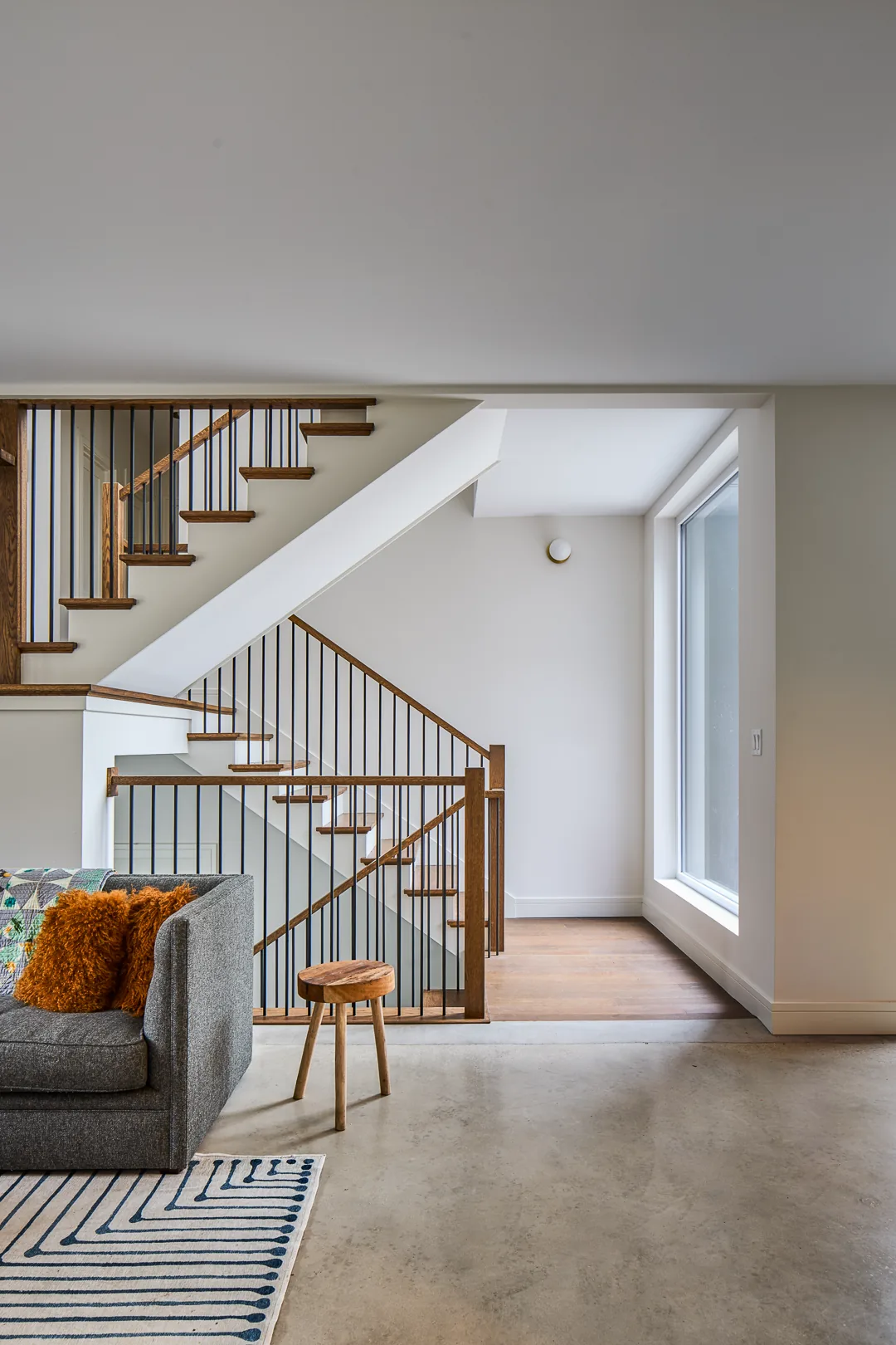 Modern staircase with wood steps and black metal railing next to a spacious window overlooking outdoors.