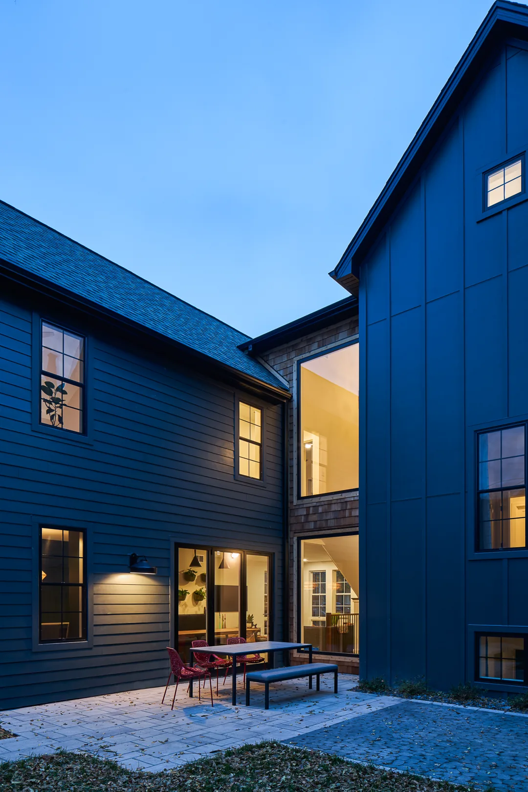Evening view of a two-story house's outdoor patio with sliding glass door and illuminated windows.