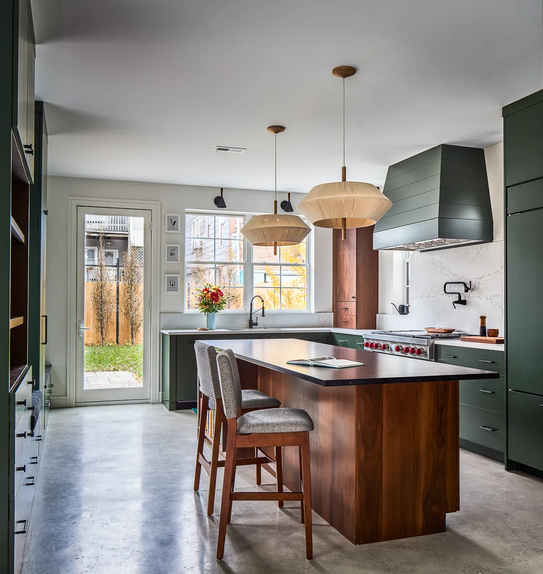 The Mozart House kitchen features a wooden island, green cabinets, and modern pendant lighting.