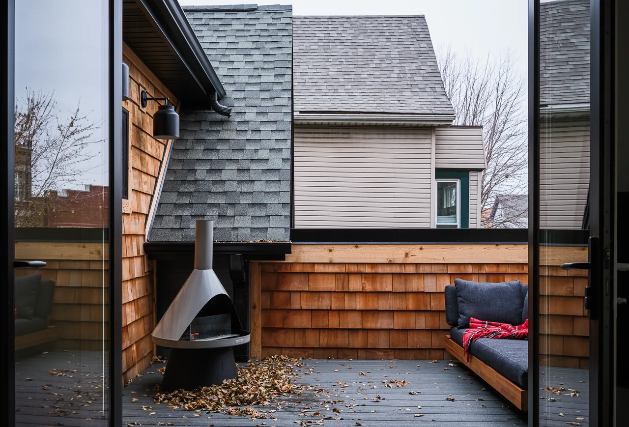 Patio deck featuring wood shingle siding, a modern outdoor fireplace, and a cushioned bench with a red blanket.