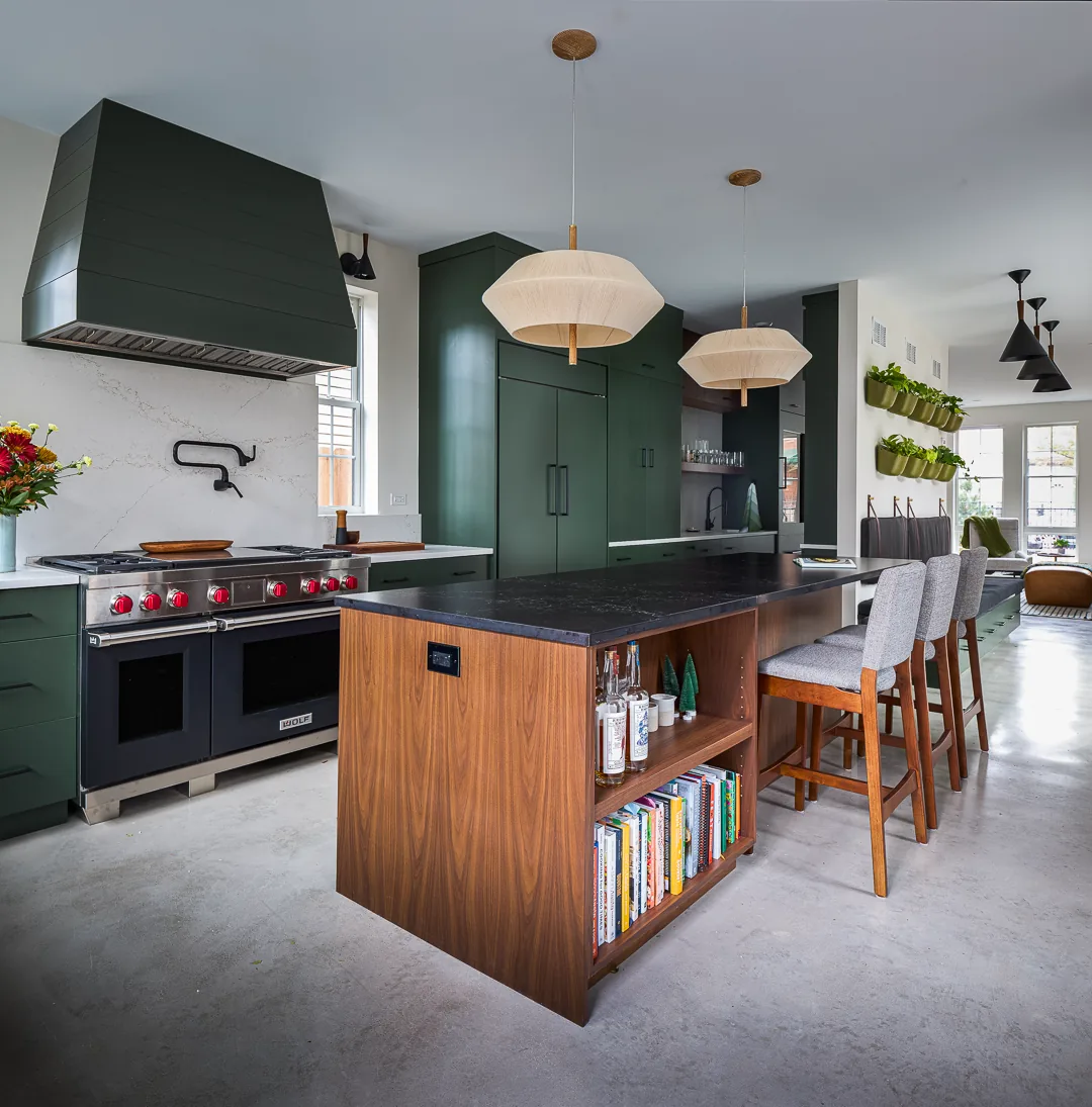 Kitchen with green cabinetry, a wooden island with built-in shelves, and modern pendant lighting over a concrete floor.