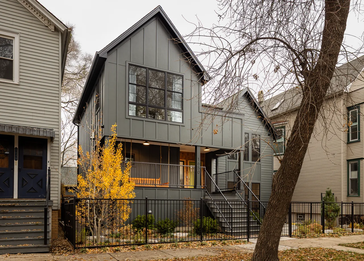 The Mozart House features vertical siding, large black-framed windows, and a black metal fence enclosing a front yard with landscaping in fall.