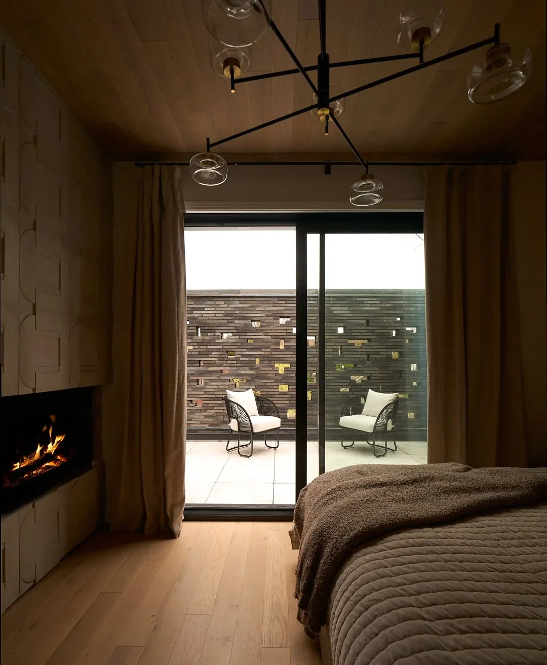 Bedroom with wood ceiling paneling, built-in fireplace, and a sliding glass door to a patio with seating.