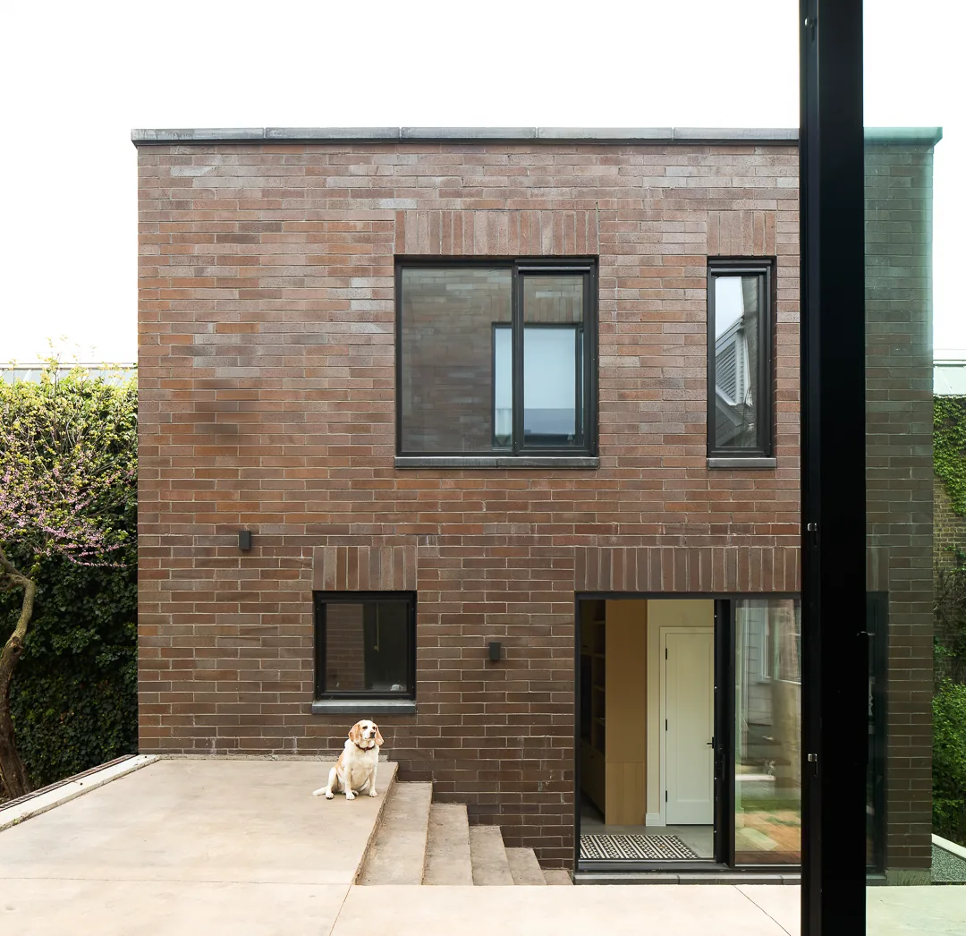 Modern rectangular brick house with black-framed windows and concrete steps leading to a glass door entry.