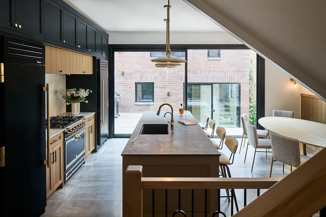A modern kitchen and dining space with a kitchen island and floor-to-ceiling sliding glass doors reveal a brick exterior courtyard.
