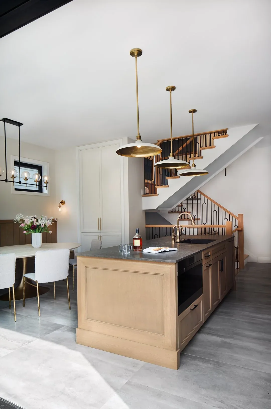 Kitchen island with brass pendant lights adjacent to a dining table and a staircase with wood and black metal railings.