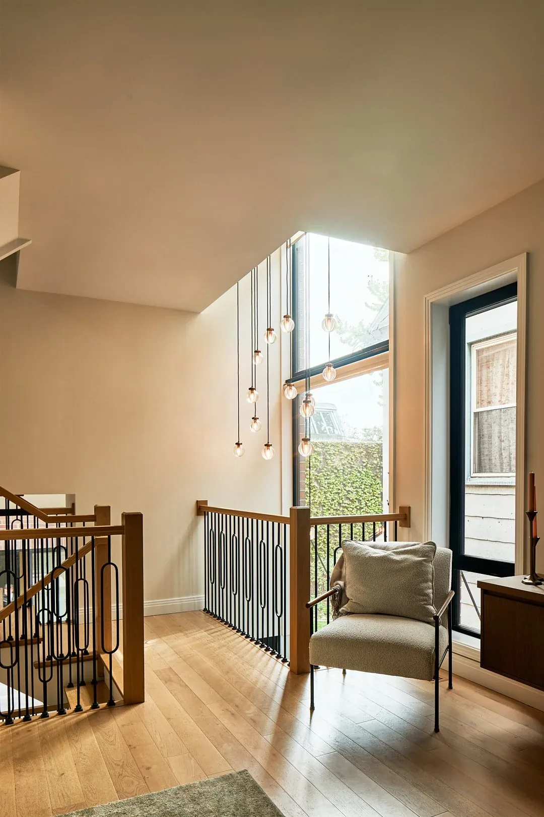 Sitting area with a cushioned chair and modern pendant lighting by a large window at the stair landing.