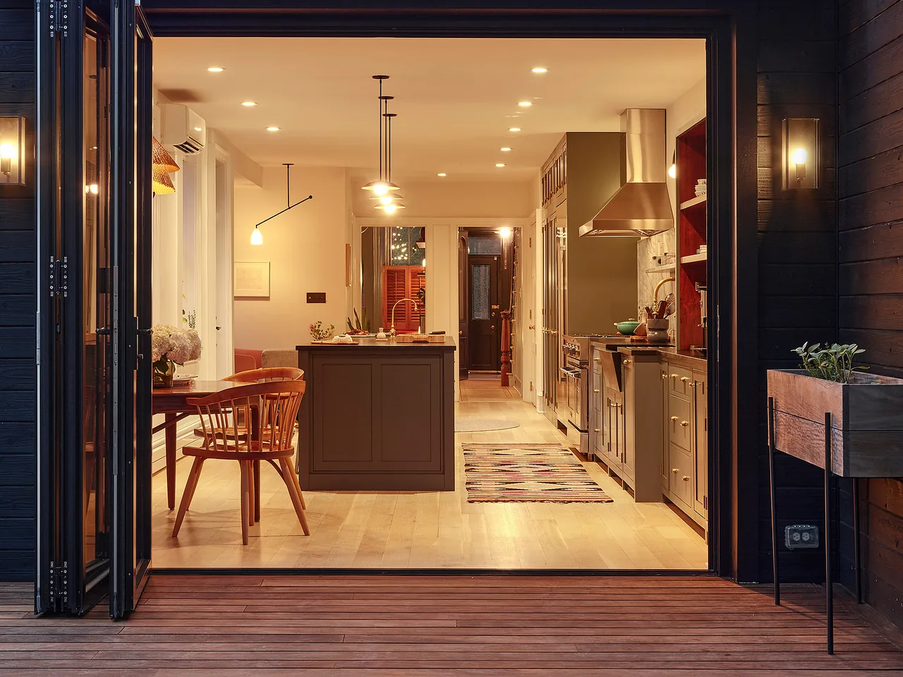 Kitchen and dining area of the Fishtown Rowhouse Addition and Renovation with an open rear folding glass door revealing wood floors and contemporary lighting.