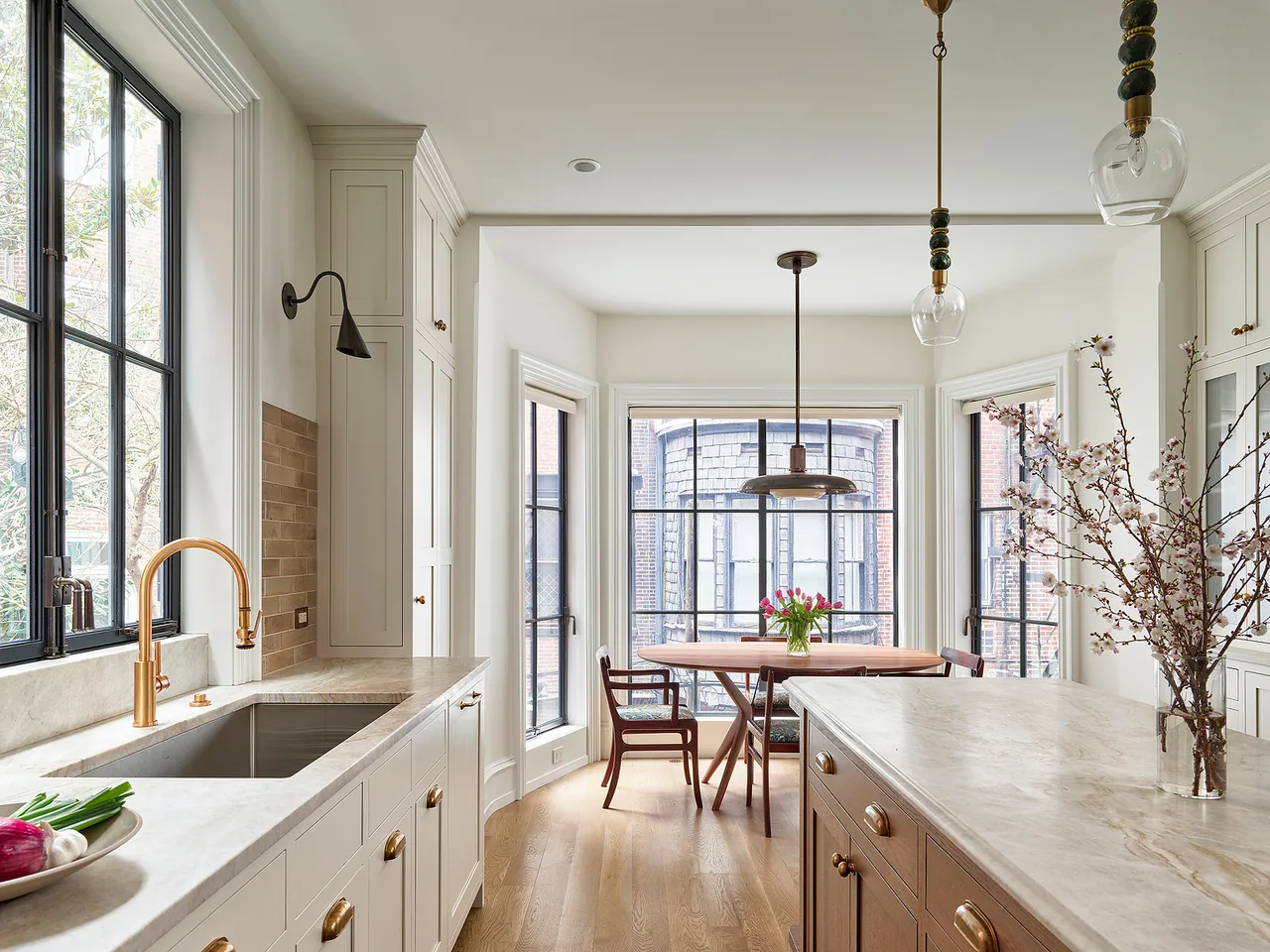The kitchen features white cabinetry, brass fixtures, large windows, and a marble island with flowers in the Fitler Square Renovation project.