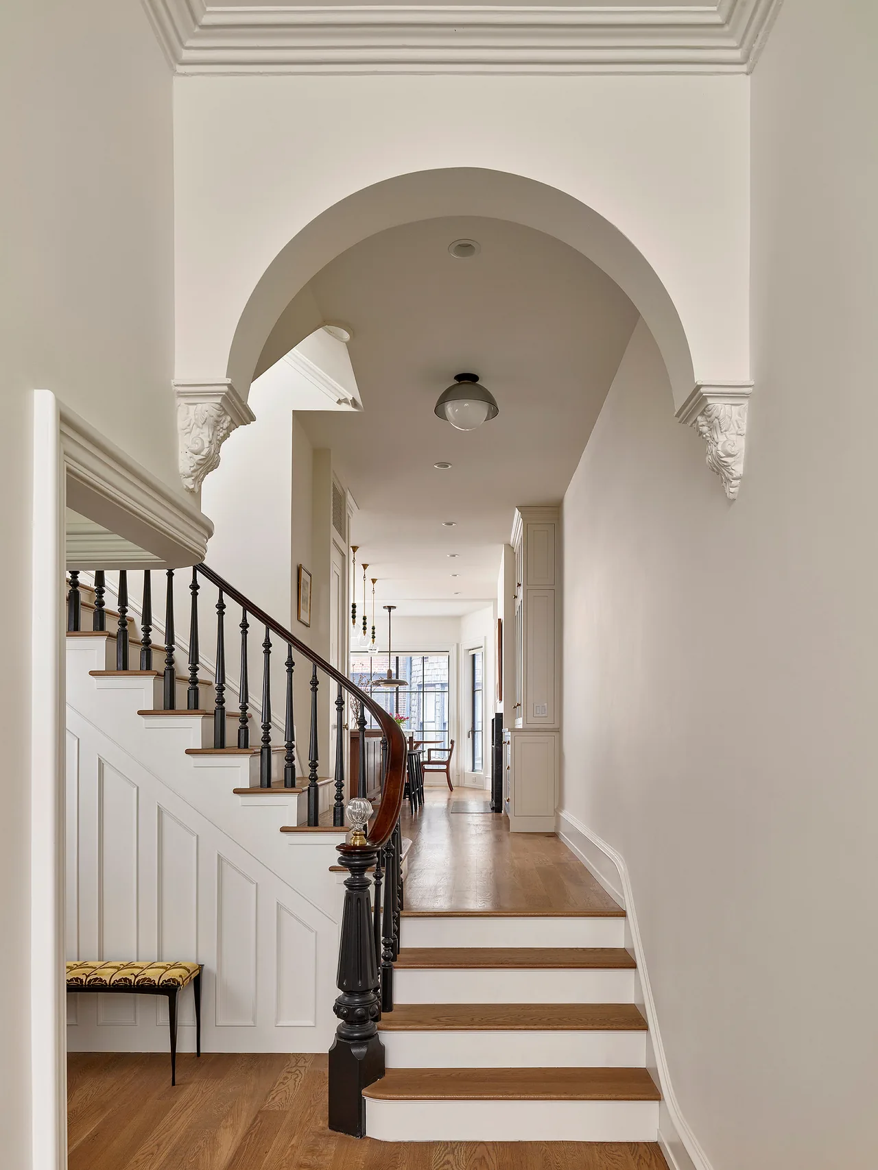 Hallway featuring a black spindled curved staircase and an arched entry with classical corbels.