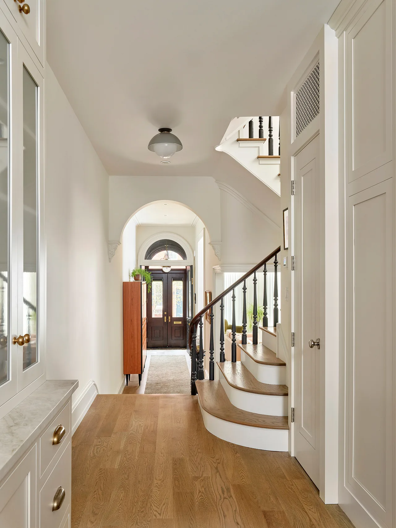 Hallway featuring a curved wooden staircase with dark balusters and an arched transom window above the front door.