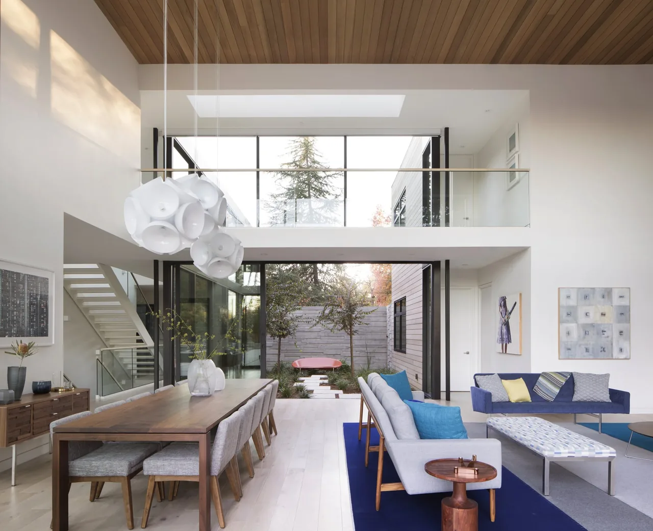 Hermosa Residence features a double-height living space with large glass doors opening to an outdoor courtyard with stepping stones.