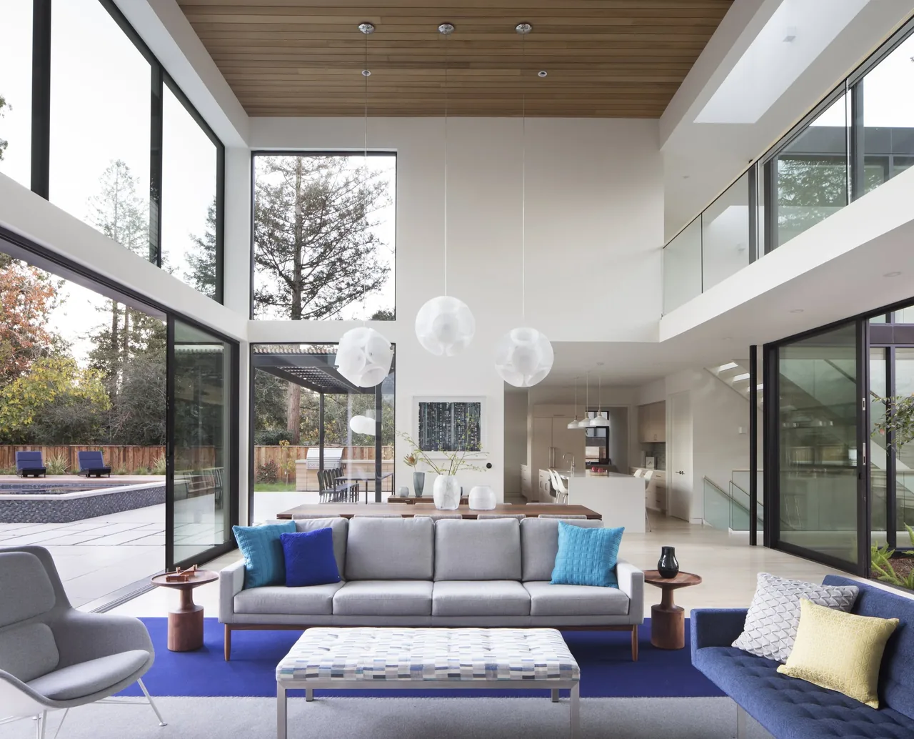 Open living space with double-height glazing and sliding glass doors overlooking pool and yard.