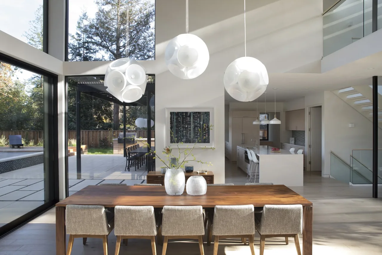 Dining area with a wood table and globe pendant lights connecting to kitchen and outdoor patio at Hermosa Residence by LTBa.
