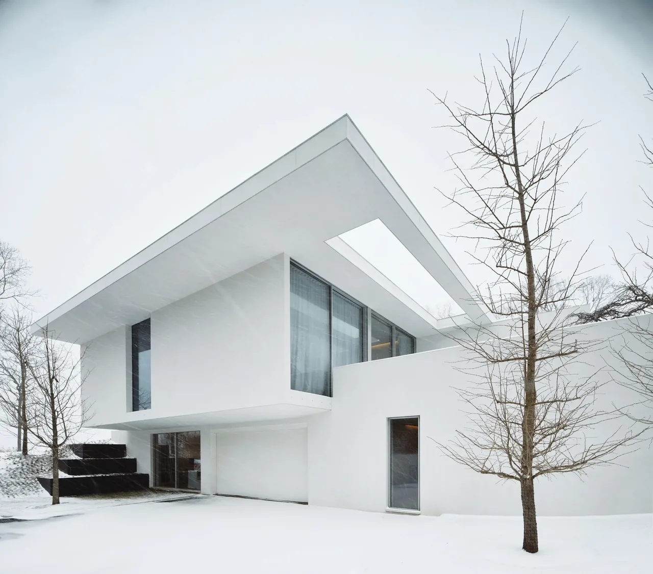 Minimalist white house featuring a flat roof with a cutout, large glazing, and stark geometry in a snowy setting.