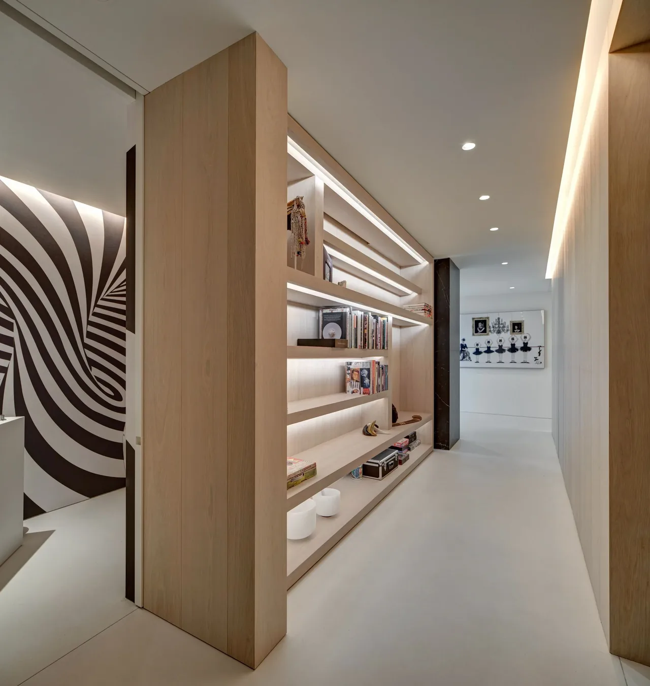 Minimal hallway features light wood built-in shelving with integrated recessed lighting, accented by a black marble panel and wall art.