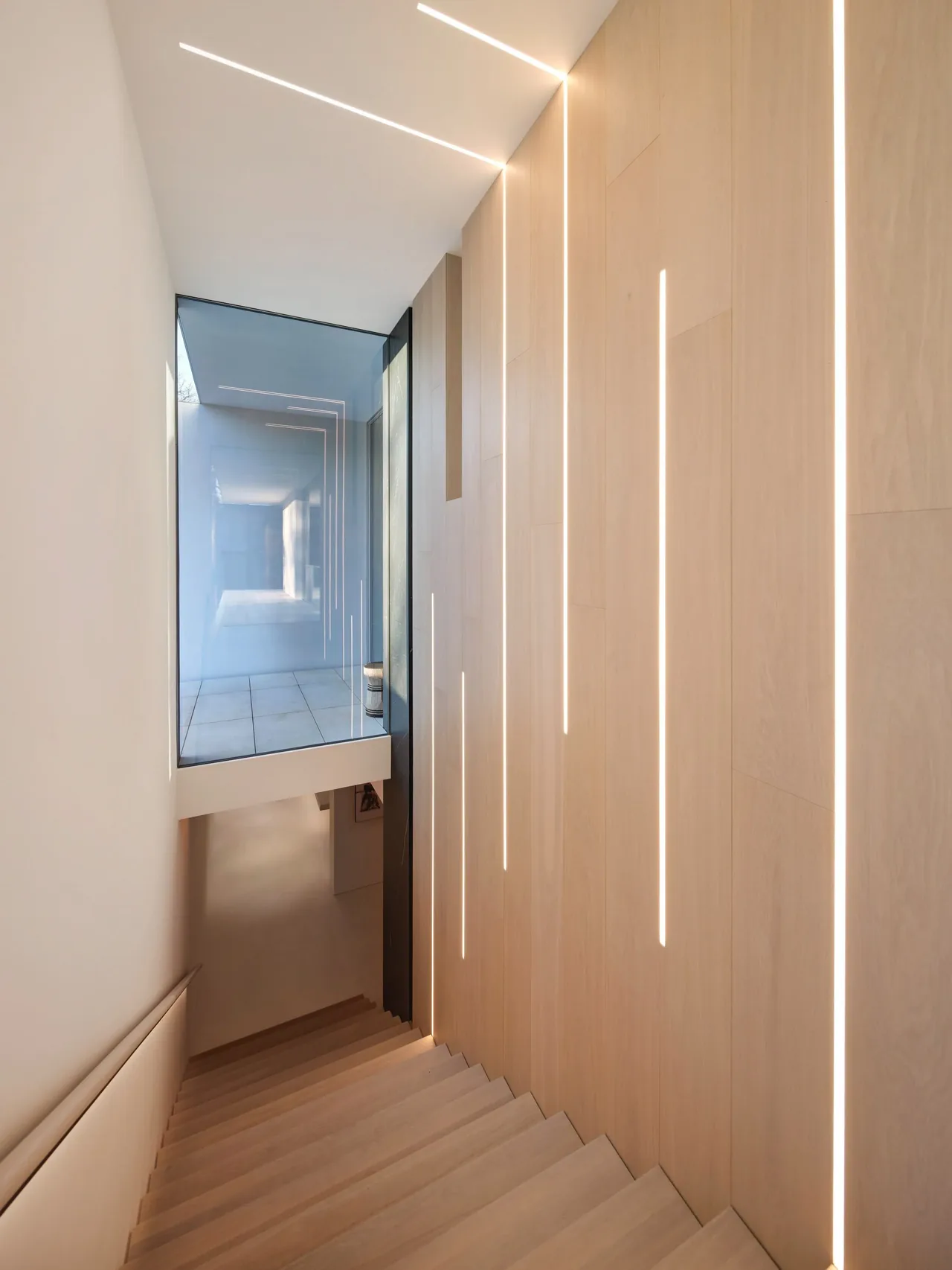 A stairwell with light wood panels featuring integrated vertical LED lighting and a large glass wall overlooking an adjacent space.