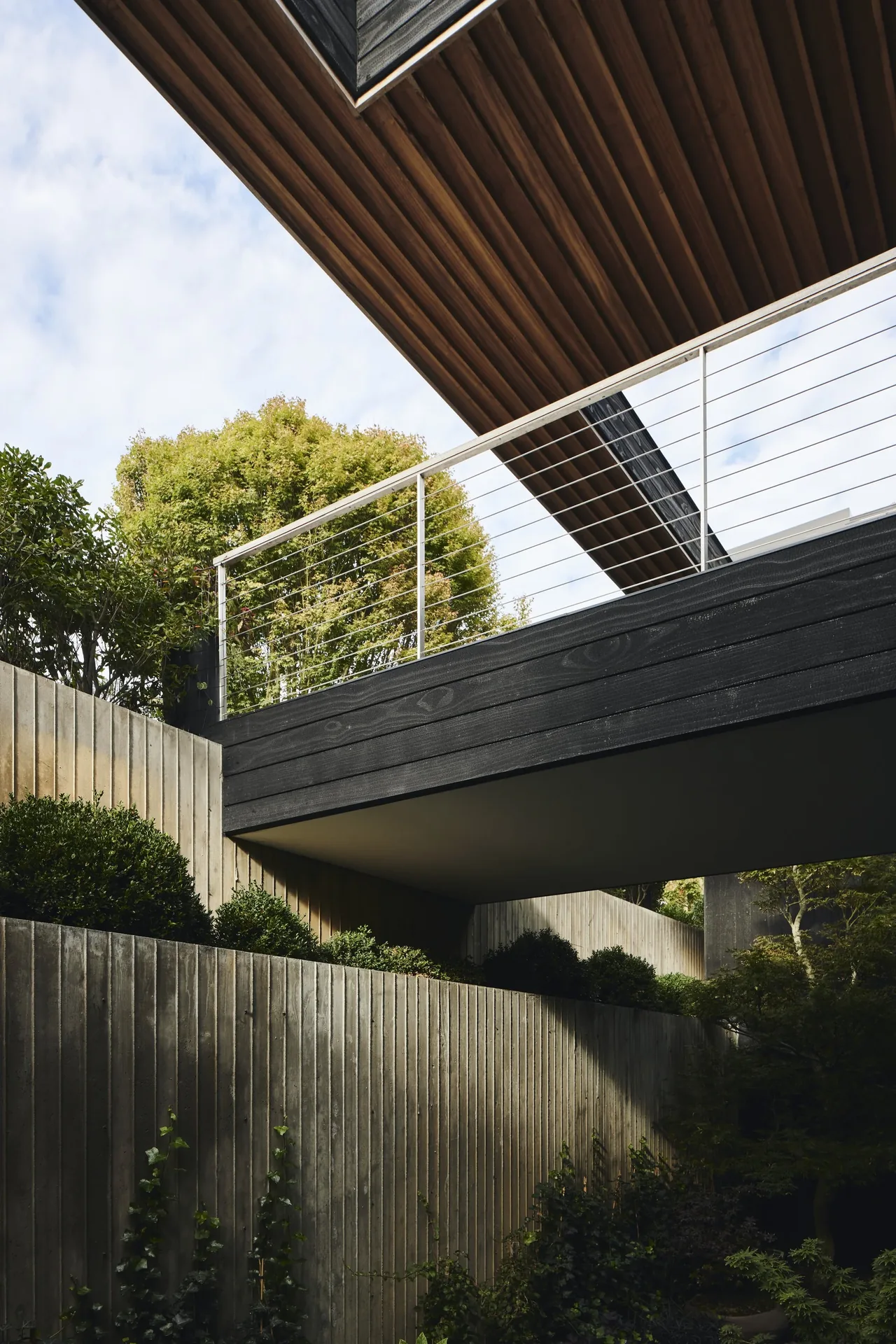 The Ocean Bluff project features an entrance bridge with blackened horizontal wood siding and landscaped vertical wood walls.