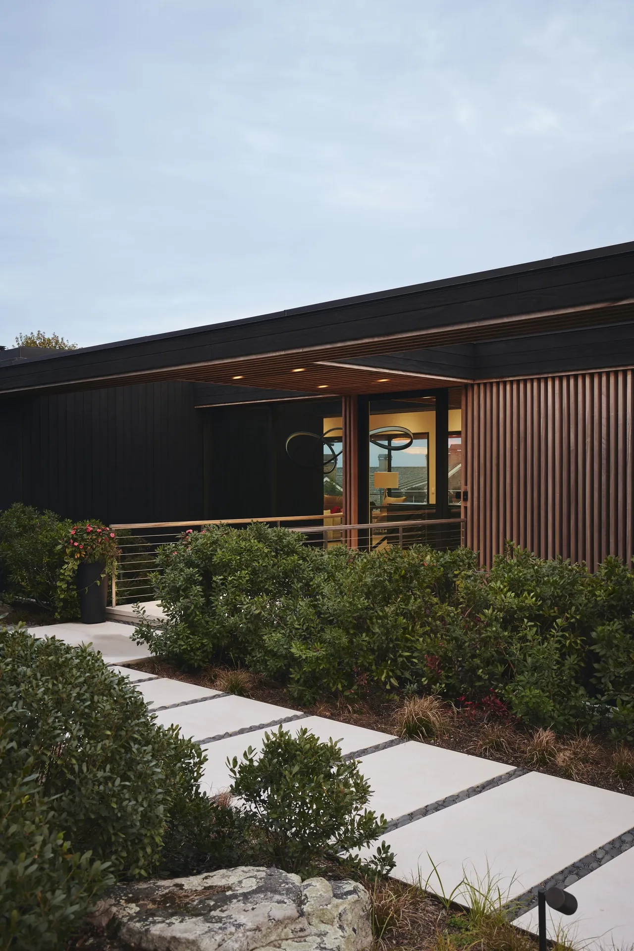 Ocean Bluff project showing the home's vertical wood siding and covered entry bridge with landscaped pathway.
