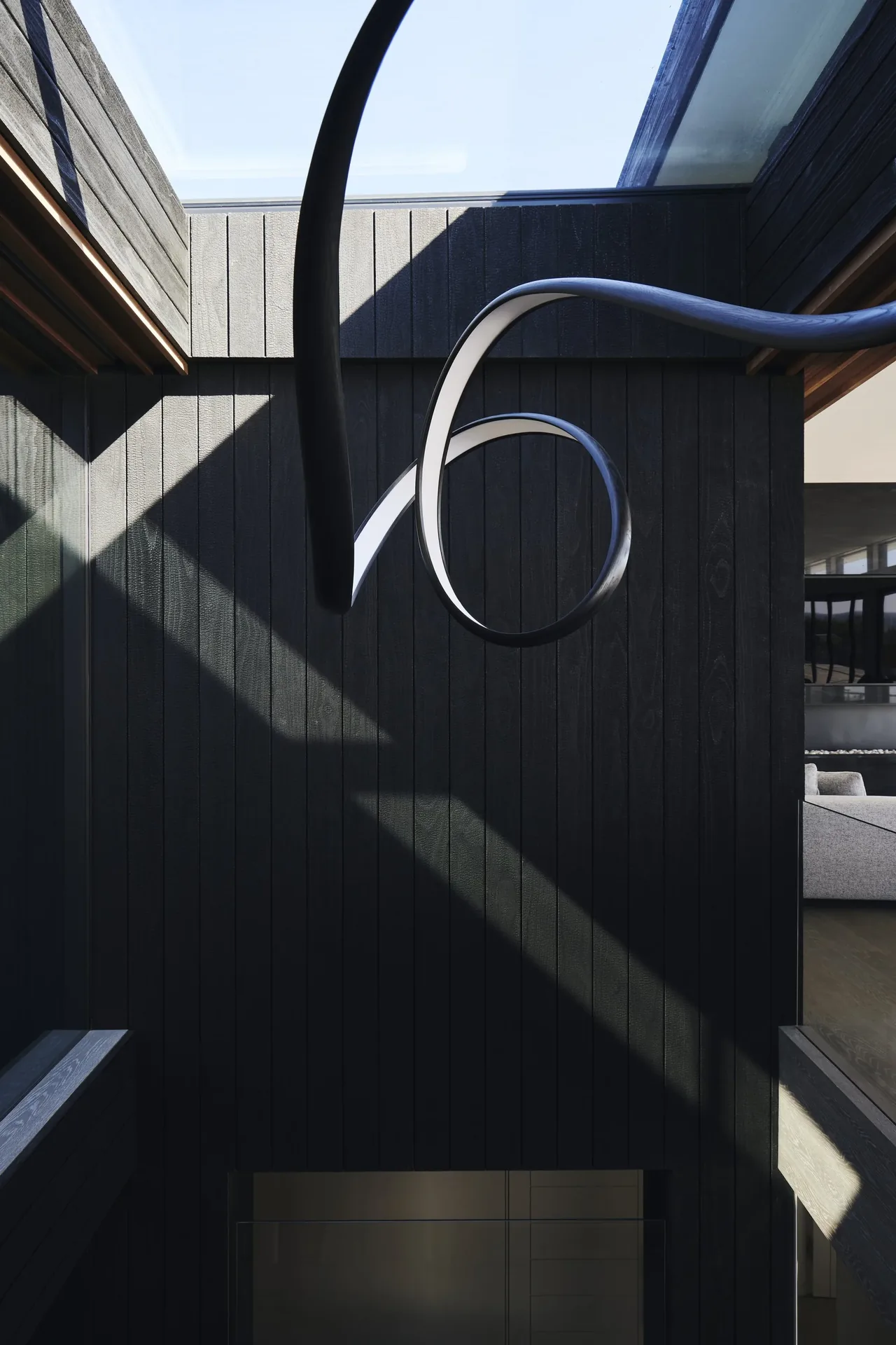 A sculptural curved black light fixture hangs in the double-height space with dark wood walls and a skylight at Ocean Bluff project.