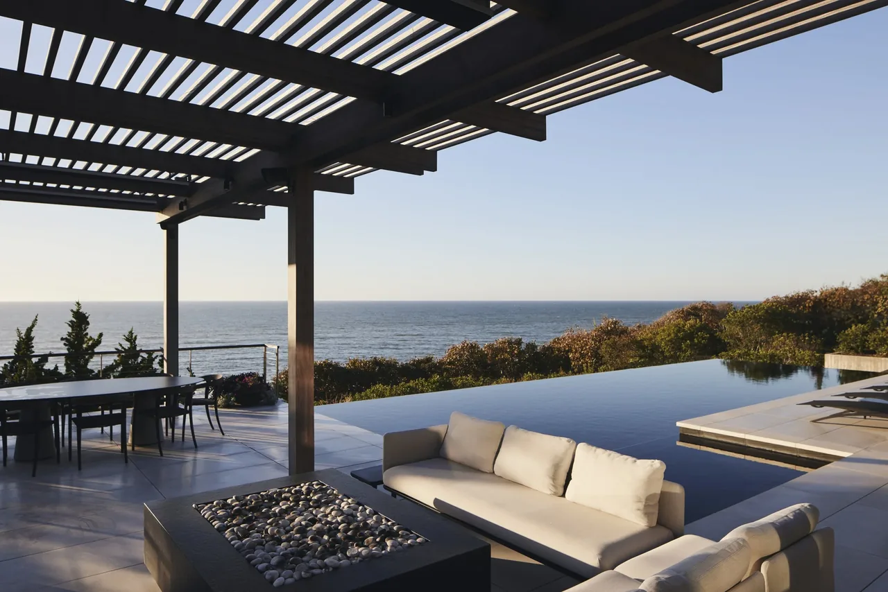 Ocean Bluff project features a covered patio with seating and dining area adjacent to an infinity pool facing the ocean.