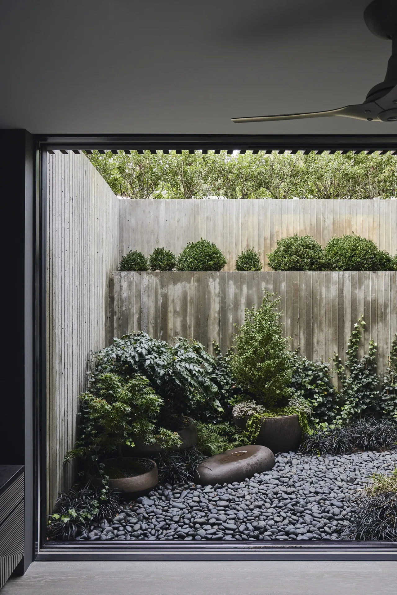 Modern courtyard garden with dense plants, river rock ground cover, and vertical wood siding walls.